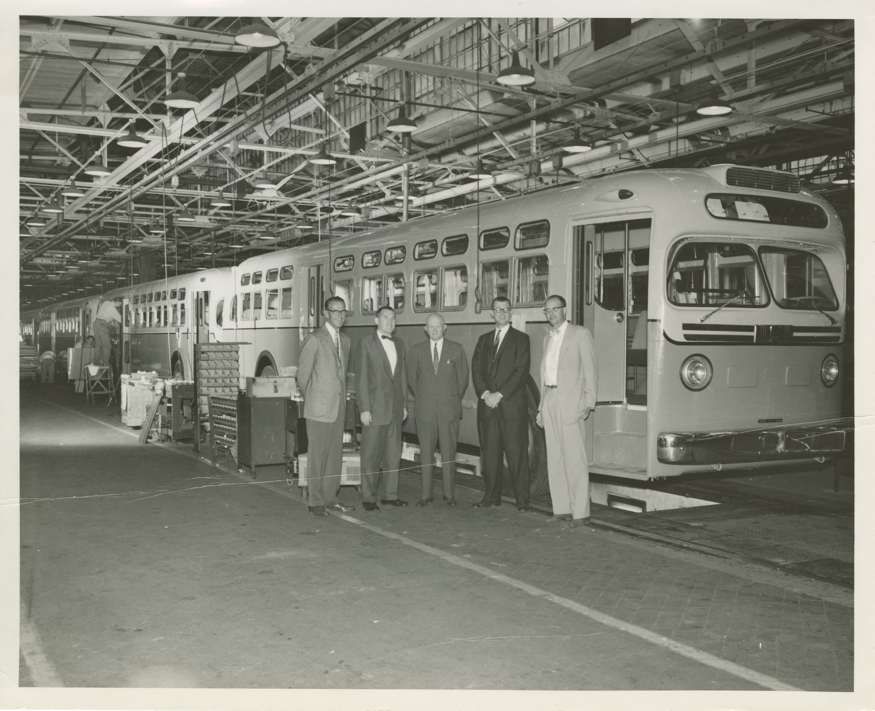 A black and white photo of Gettler with colleagues at a bus manufacturing facility, circa 1950s.