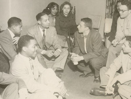 Black and white photo of Berry sitting on the floor in conversation with several young men and women