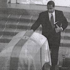 A black and white photo of a man with his hand on a casket