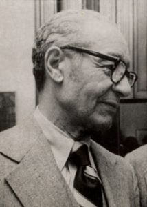 Black and white profile view of Berry standing and wearing black glasses and a suit
