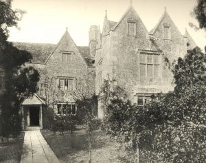 A black and white photo of the front of the manor, a large gray stone estate with large trees 