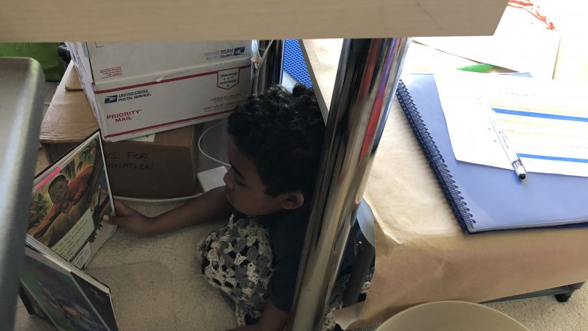 Boy reading underneath a desk.