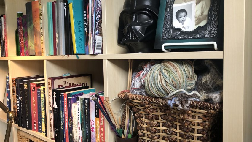 Yarn and knitting needles on bookshelf.