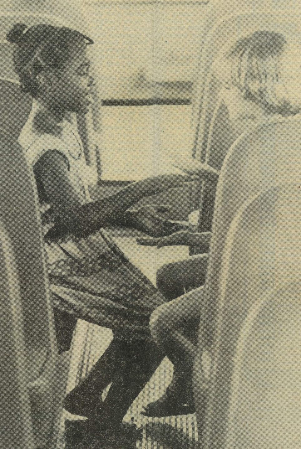 Newspaper image of young girls (one Black and one White) playing a hand game sitting across from each other on the bus.
