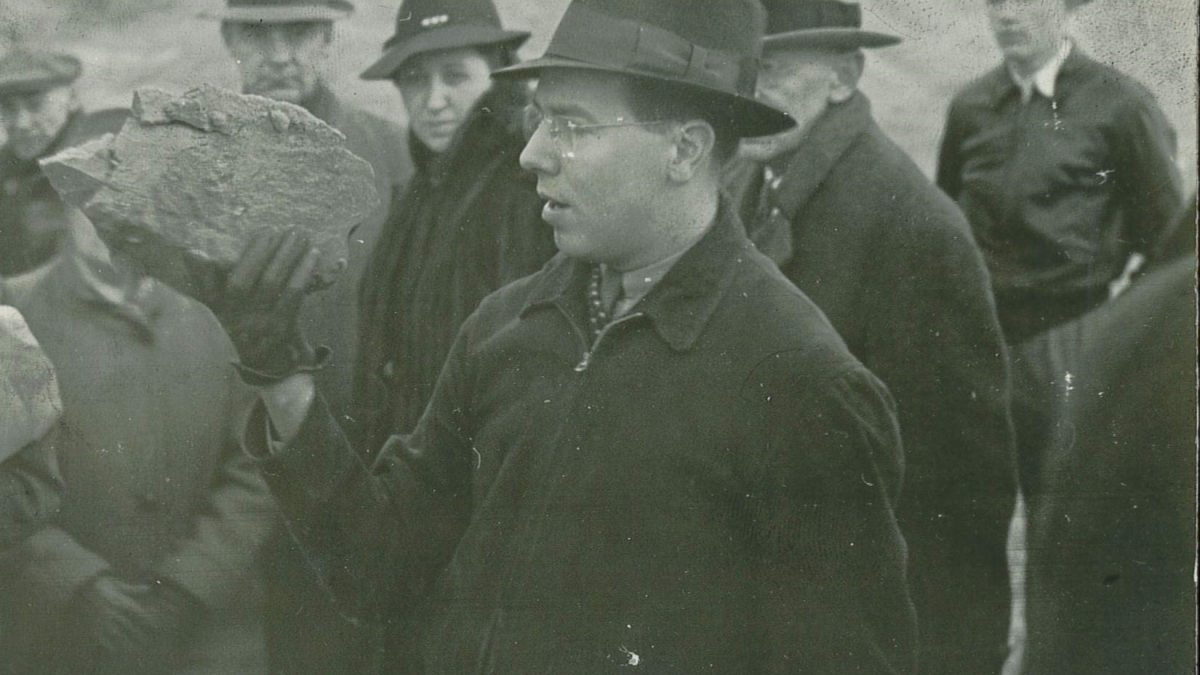 Photograph of Dr. Kenneth Caster showcasing a rock fossil to a group of students outside at an unknown location.