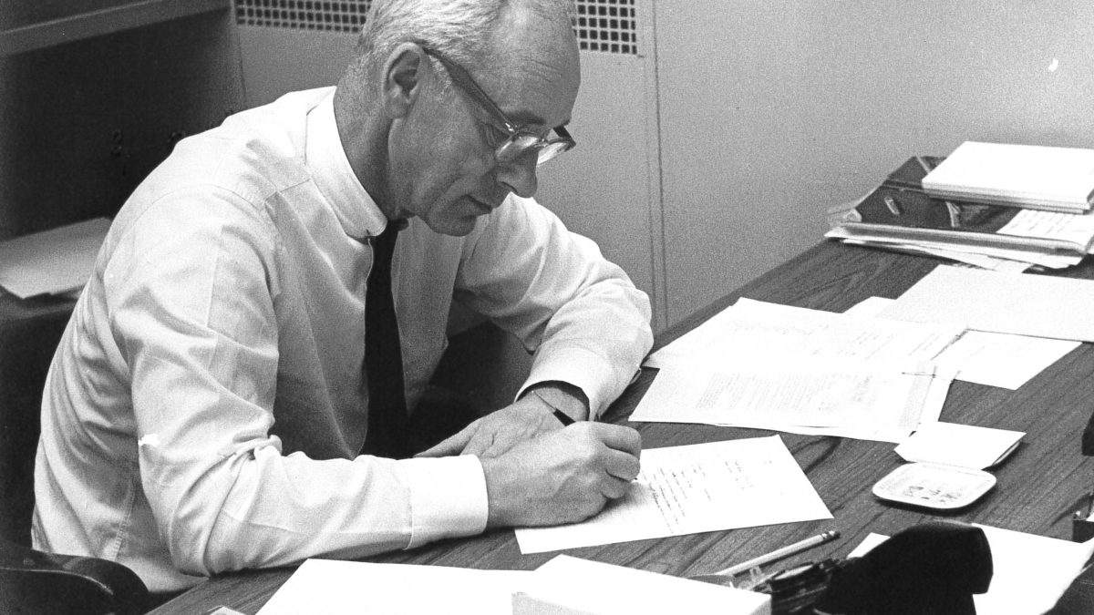 Photograph of an older Von Rosenstiel sitting at his desk looking down at a piece of paper he is writing on. From 1964