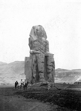 A black and white photo of a group of travelers on horses next to the Colossus of Memmom in Egypt