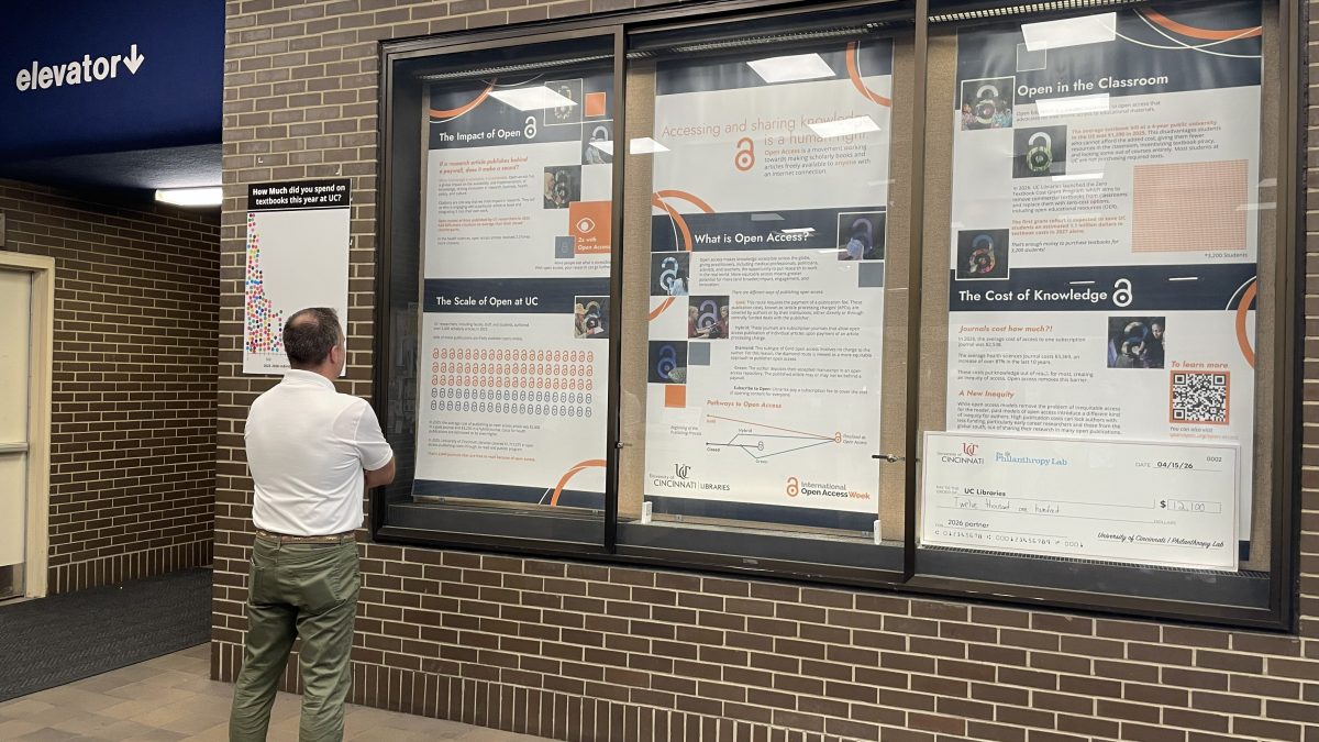 Person looking at a library exhibit on Open Access.  The exhibit is three posters in a glass cabinet.