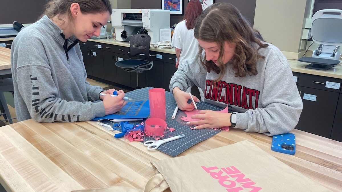 Two people cutting vinyl in the MakerLab to create a custom tote bag project.