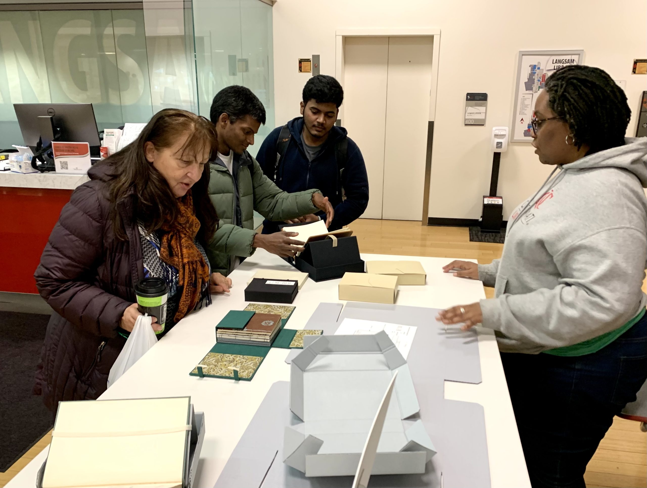 Three library visitors and Hyacinth at the table displaying various enclosures.