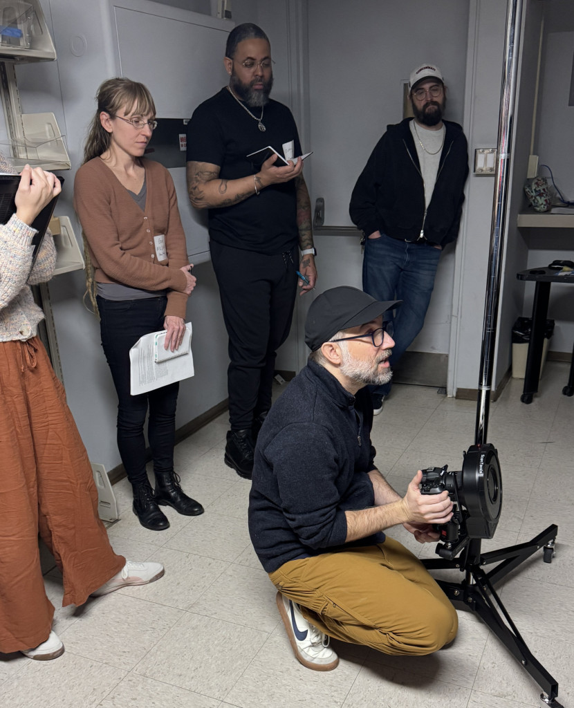 Person kneeling behind a camera with four other people standing behind him.