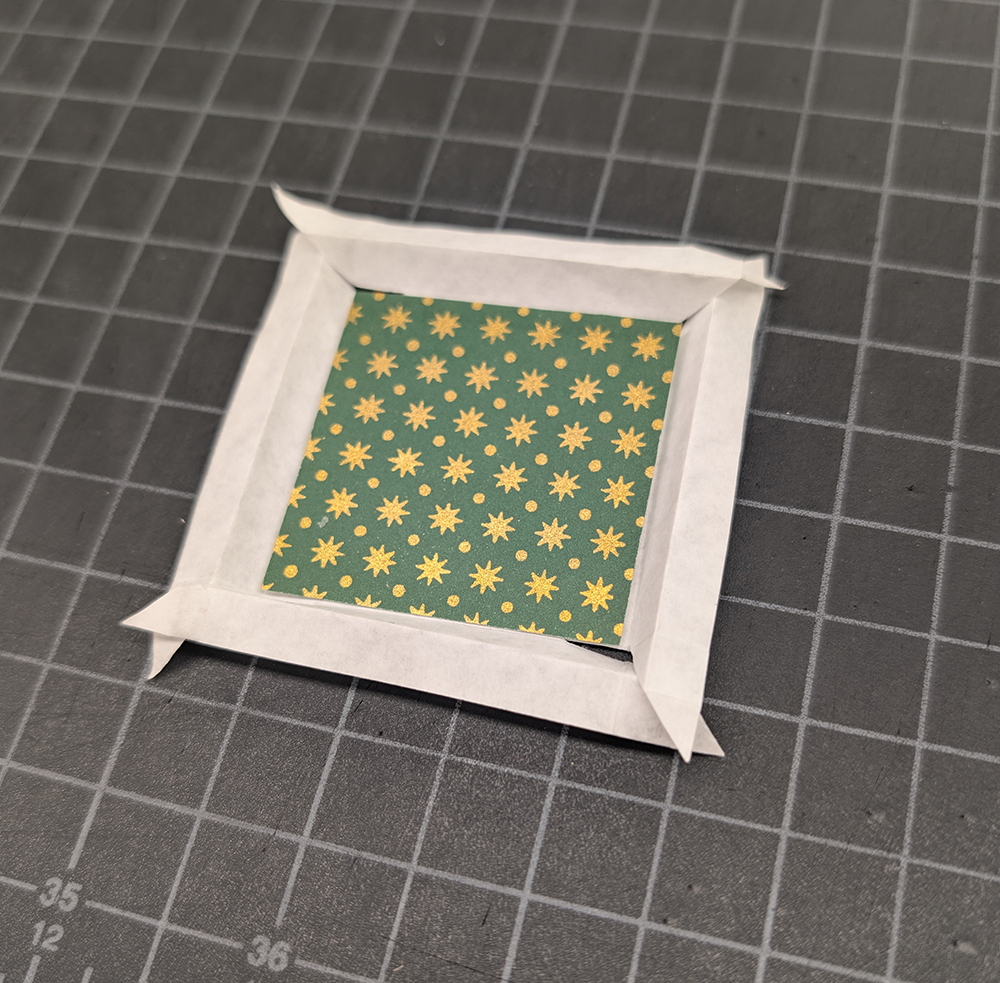 Small piece of green and gold decorative paper with a paper folded around it.