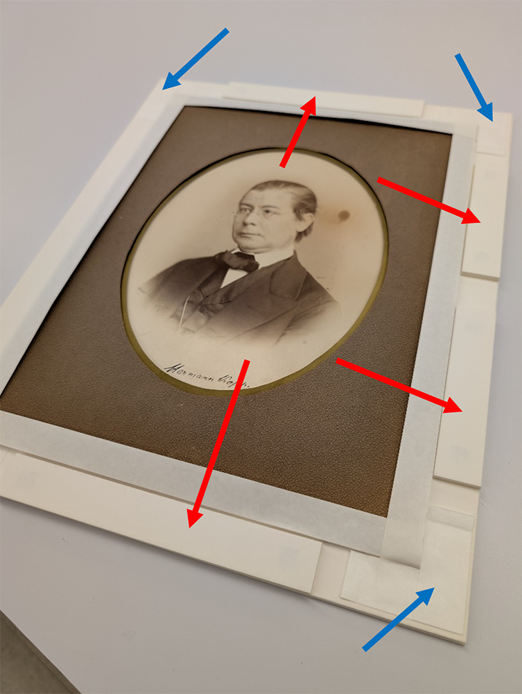Image of the photograph in the sink mat with red arrows pointing to the sink mat elements along the right edge and bottom and blue arrows pointing to the tape holding the tabs of the paper cradle in place at the corners.