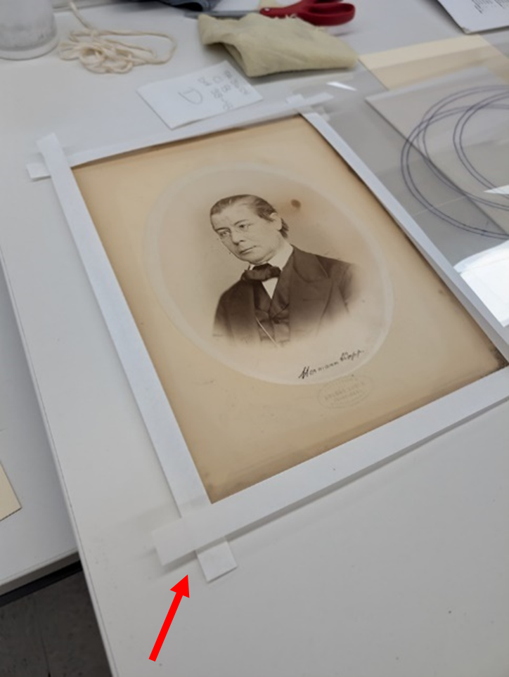 The photograph in a paper z-fold cradle with a red arrow pointing to the bottom left corner where the tabs of the cradle overlap.