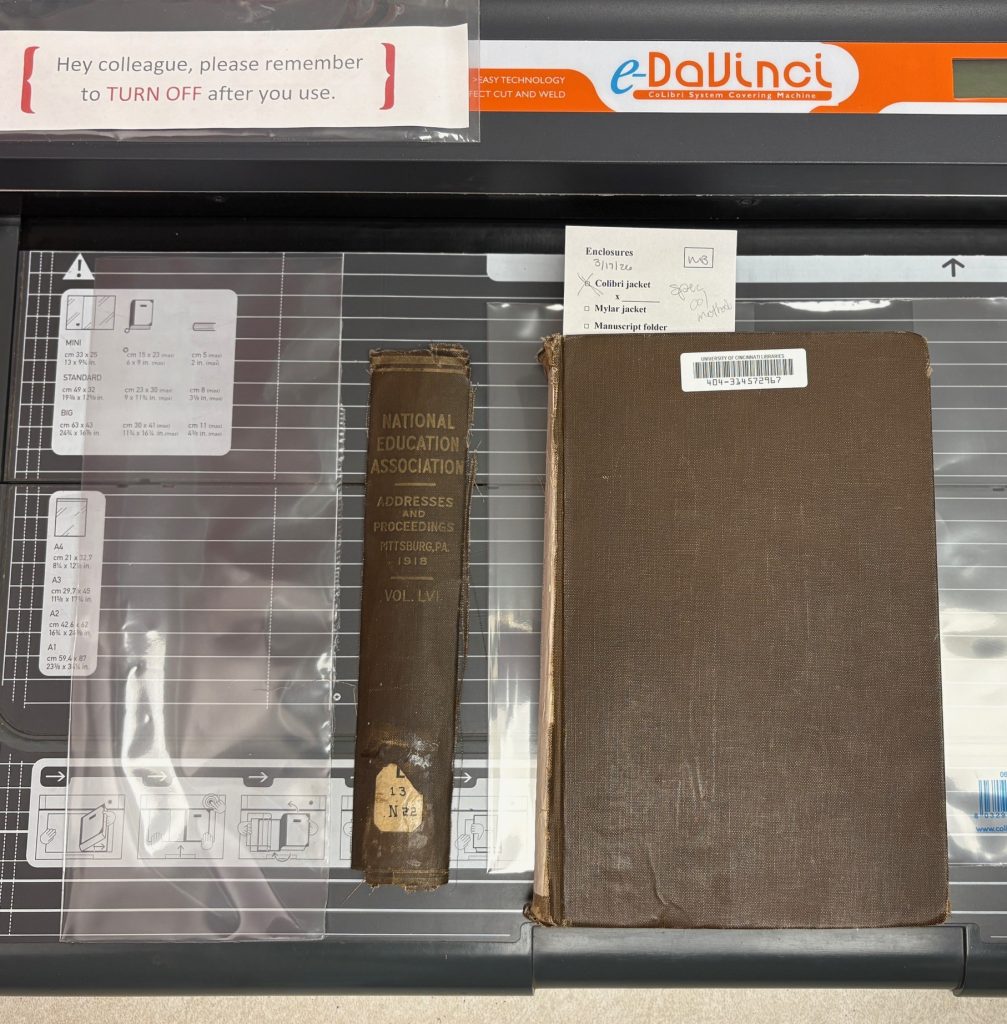 Detached spine and book are sitting on the bed of the CoLibri welding machine next to plastic sleeves to use for the jacket.