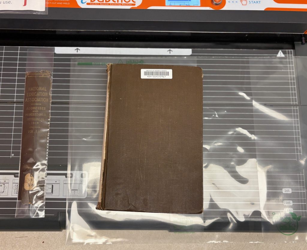 The encapsulated spine pocket sits next to the closed book.  The book is sitting on top of an un-used CoLibri jacket that is taller than the book.