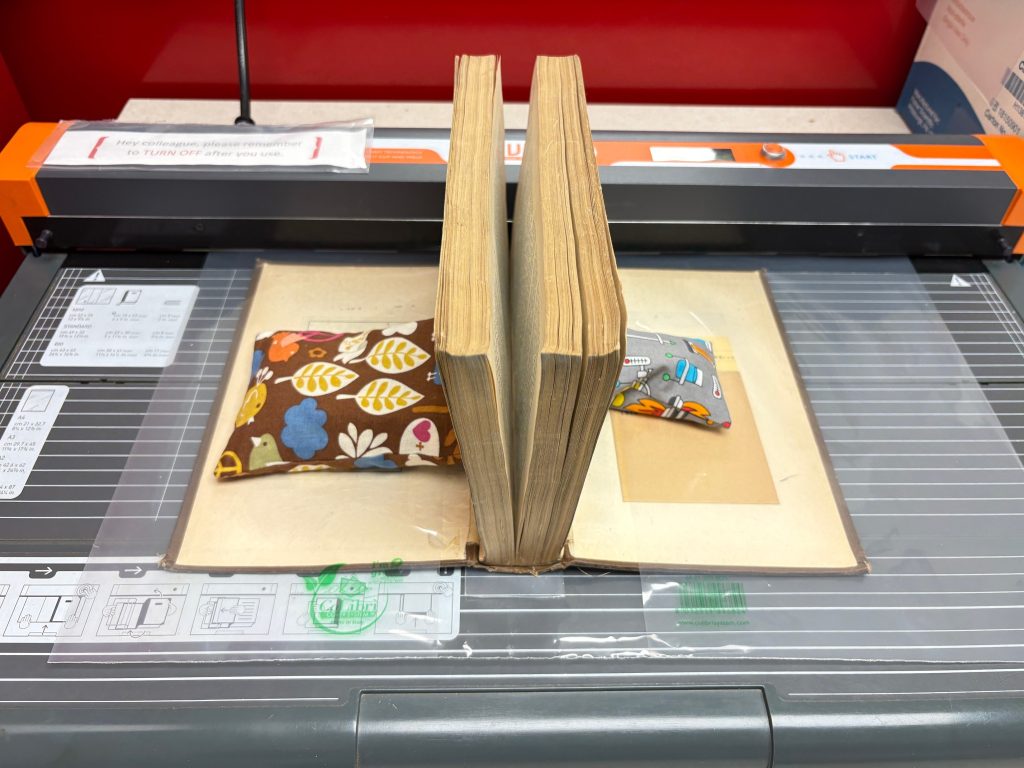 The book is laid cover side down with the covers opened on each side with bags of weights to hold it in place. The pages are closed, sticking upright with the help of the weights.