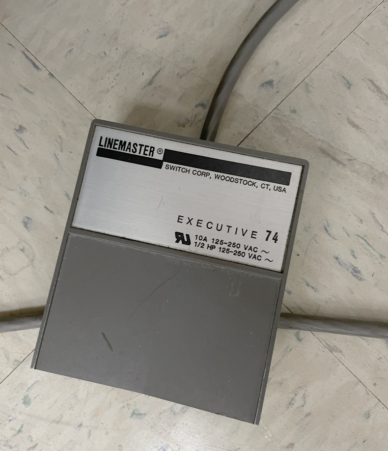 Grey foot pedal resting on the ground, connected to a cord.