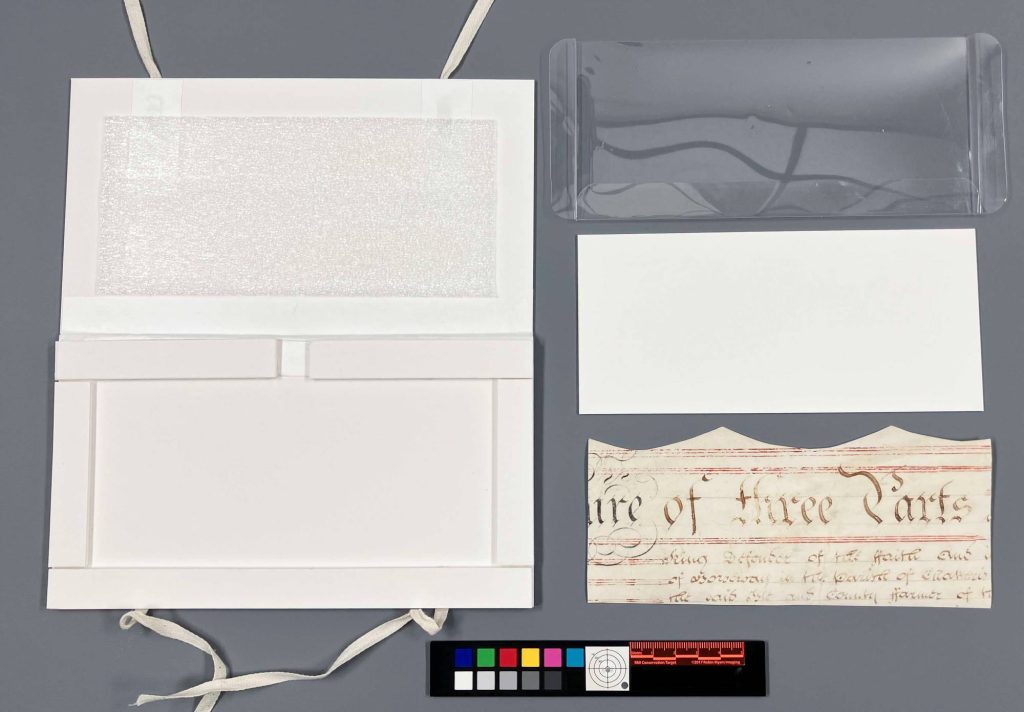 Small matting system, opened, with ethafoam on lid, mylar and mat board supports and small piece of a parchment document.