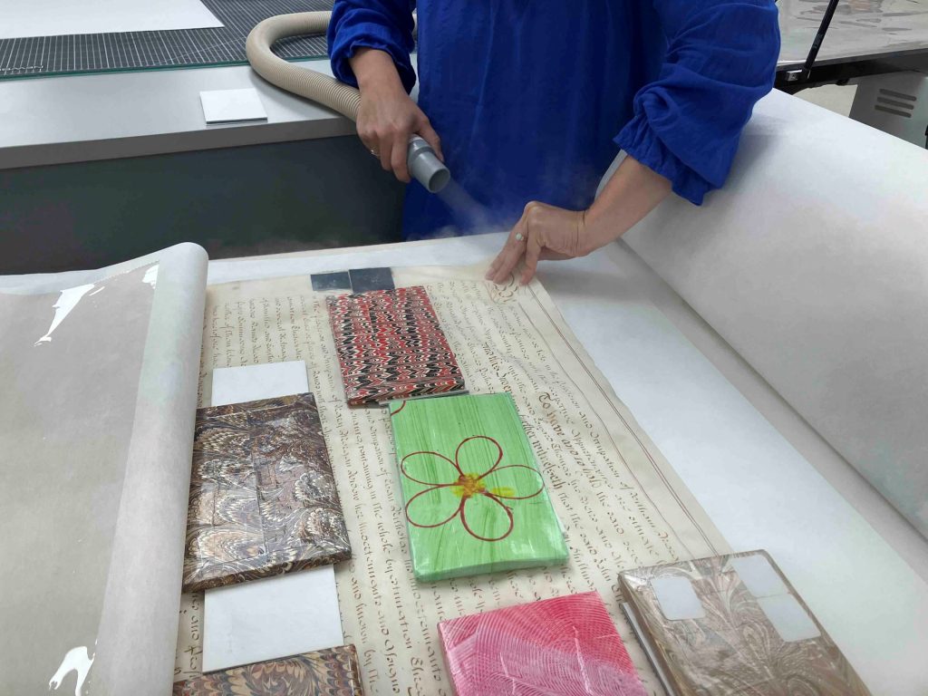 Conservator holding humidifier nozzle to locally humidify parchment document as it's being flattened on the suction table.