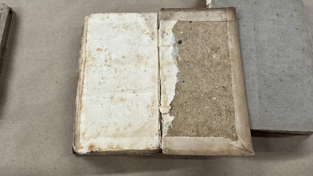 Historical boarded binding example with pastedown partially missing, leaving the board mostly exposed.