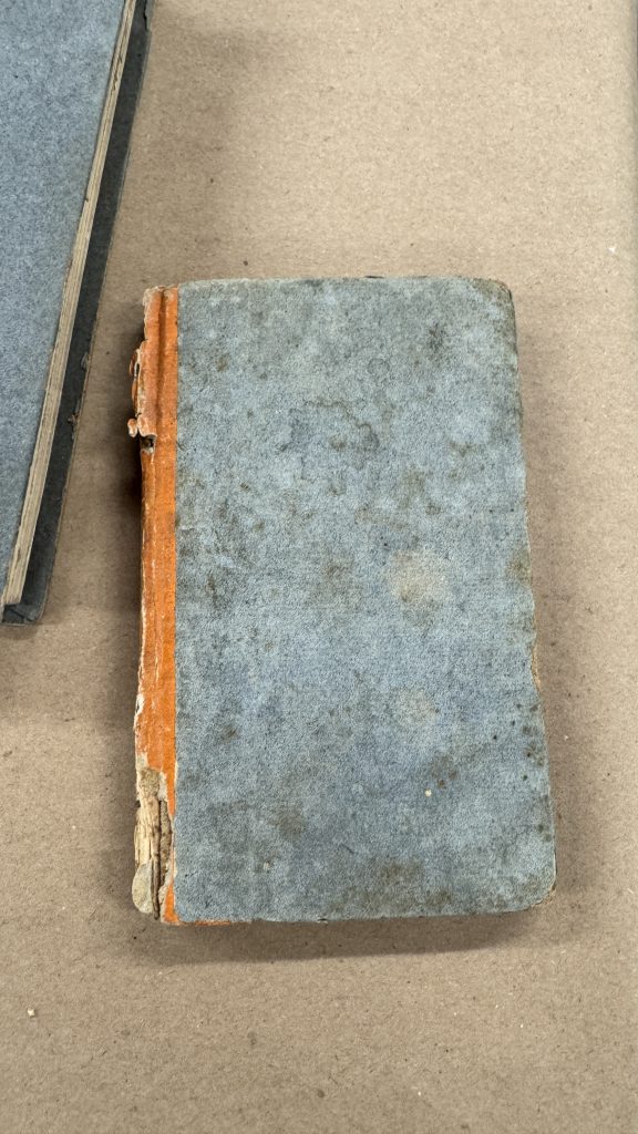 Quarter bound boarded binding with red paper on spine and blue paper covering the boards.