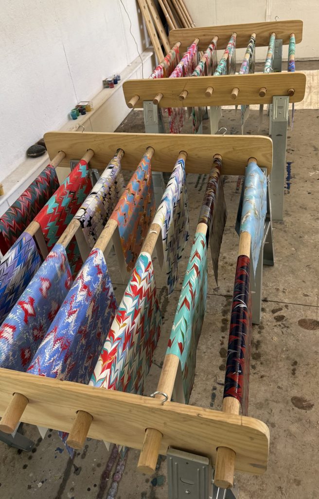 A collection of marbled paper hanging to dry on large dowel rods between saw horses.