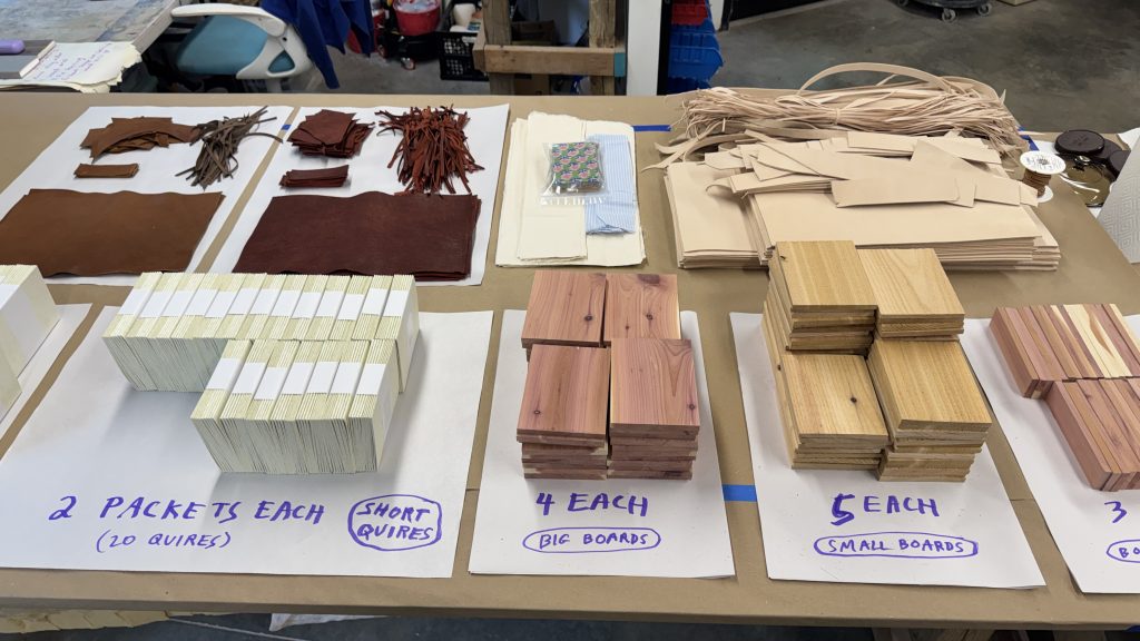 Table with neat stacks of prepared materials for workshop, including boards, leather and textblocks.