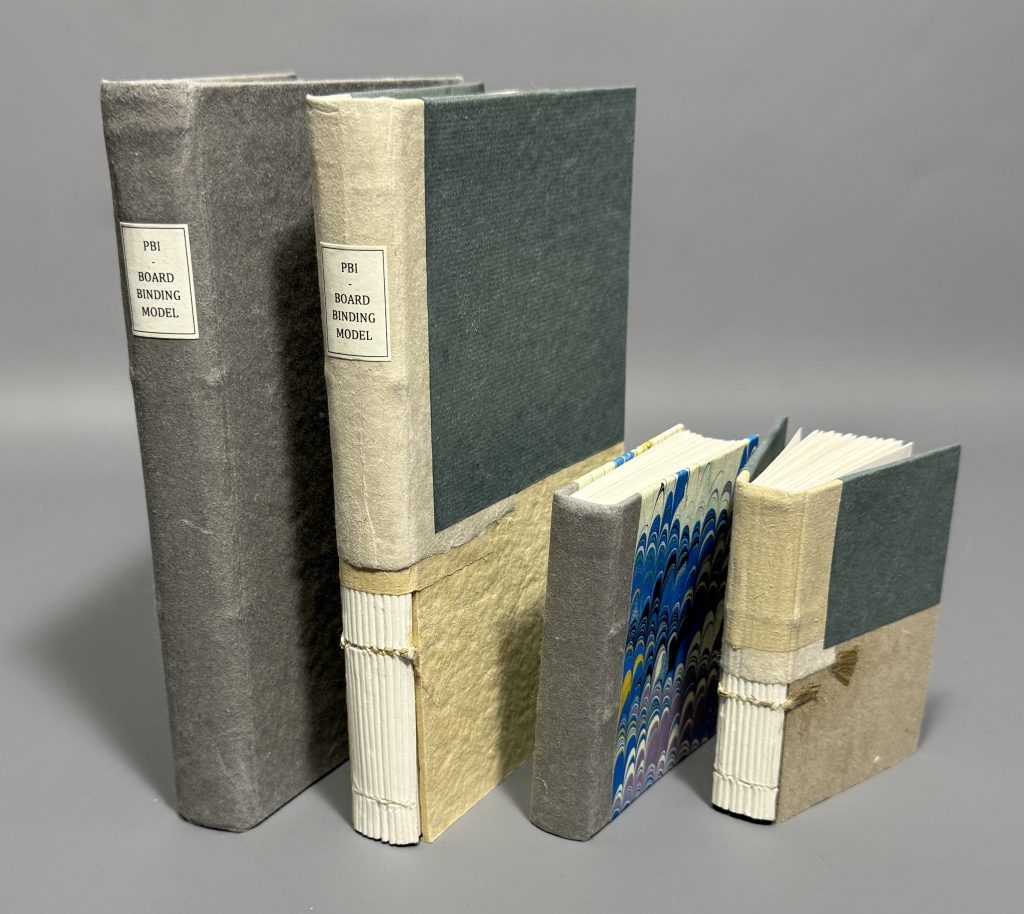 Four boarded binding models: grey paper-covered binding, quarter binding cutaway model, quarter binding "extra" boarded binding model with marbled paper and grey paper on the spine, and a small quarter binding cutaway model.