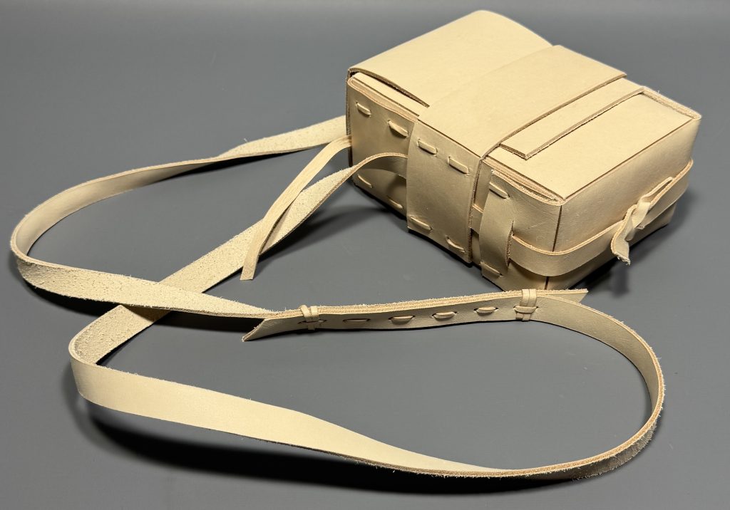 Beige leather satchel with strap that has been woven together with strips of leather to extend the length.