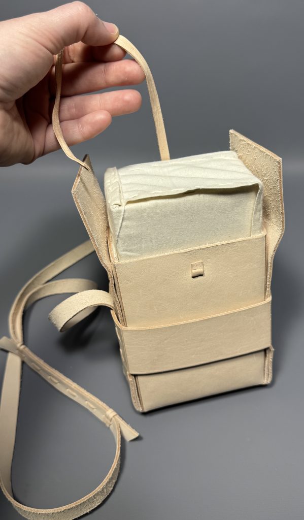 Demonstrating the leather pull string in the satchel which is used to pull the book out of the satchel.