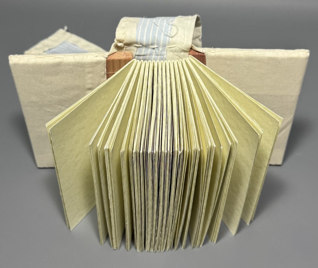 A view of the book opened to show how the textile over-cover is sewn around the covers of the book and the tab is sewn to the main overcover piece.