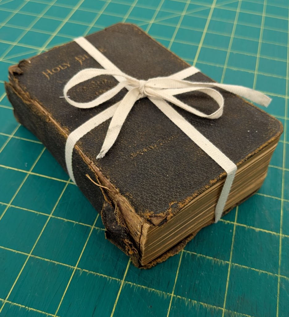 Small damaged cloth bound bible tied with cloth ties to keep it together.