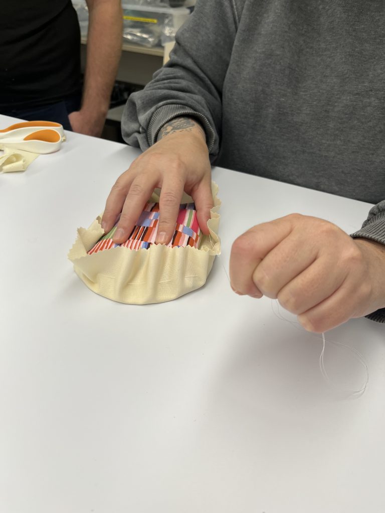 Cloth being cinched around an oval mat board the shape of the base of the hat mount.