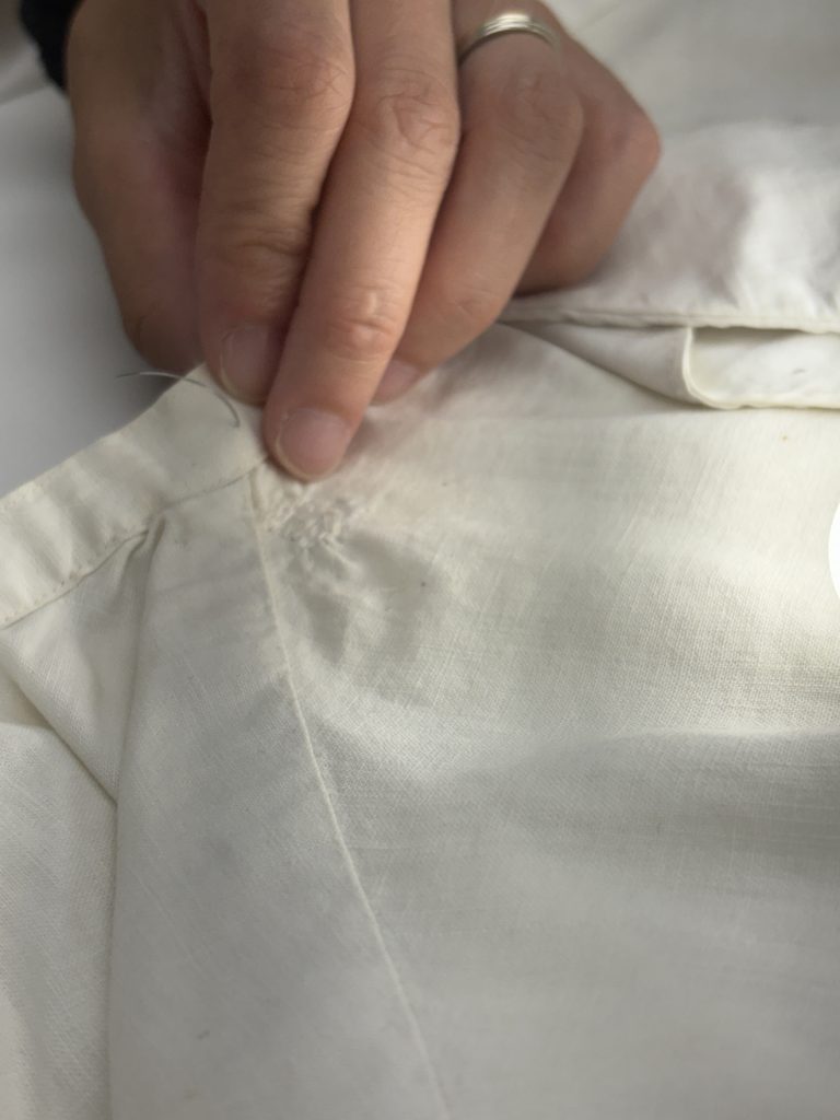 Close up of white nurse's uniform being repaired along the collar.
