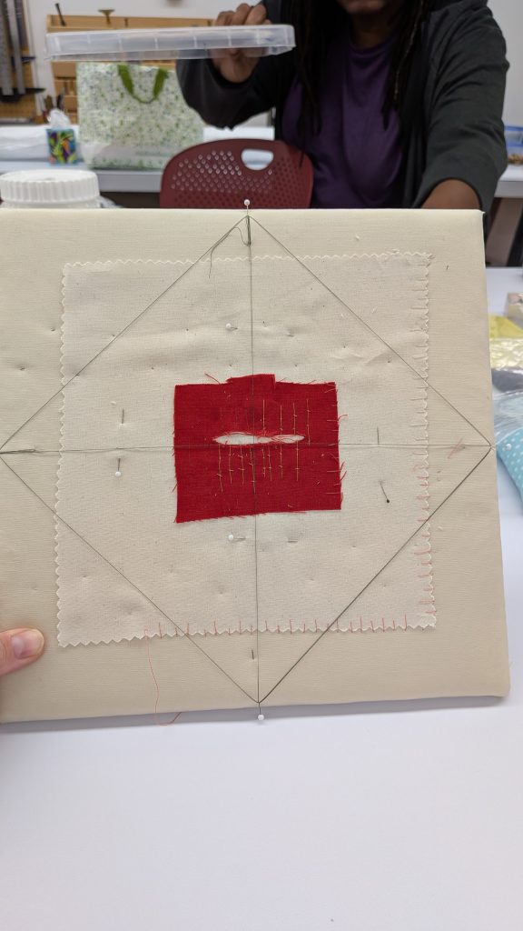Red fabric with tear repaired and mounted to a padded backing board for stability.