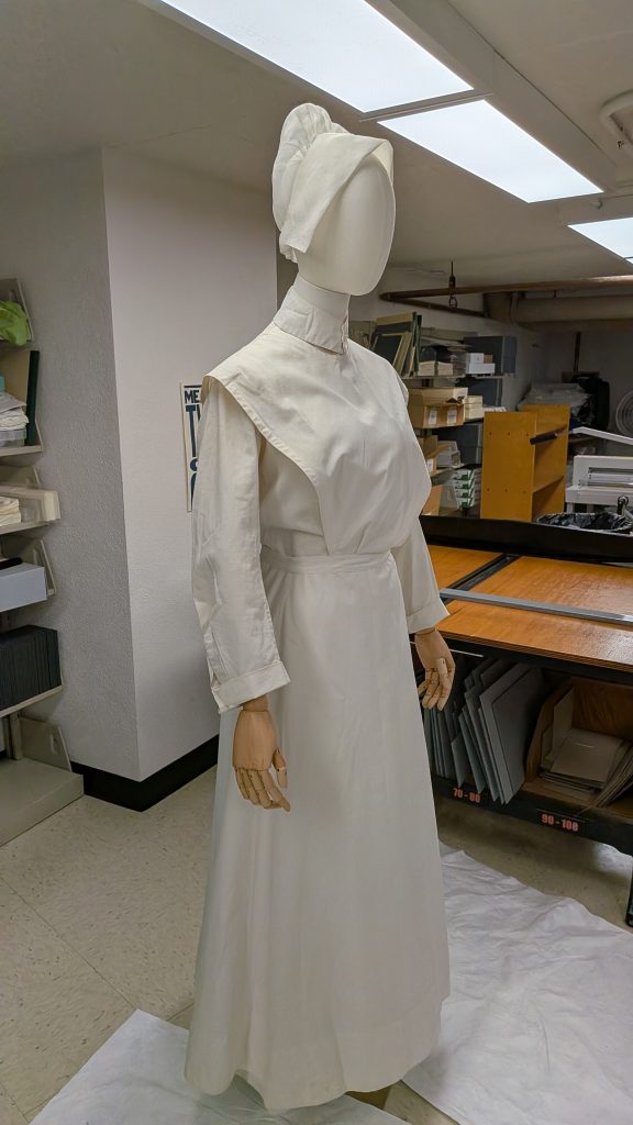 Mannequin dressed in nurse's uniform, apron, and hat.
