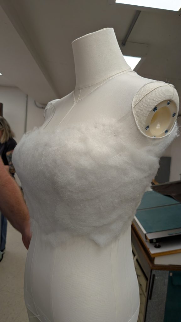 Mannequin in the process of being padded out with batting to create a better shape to hang garment.